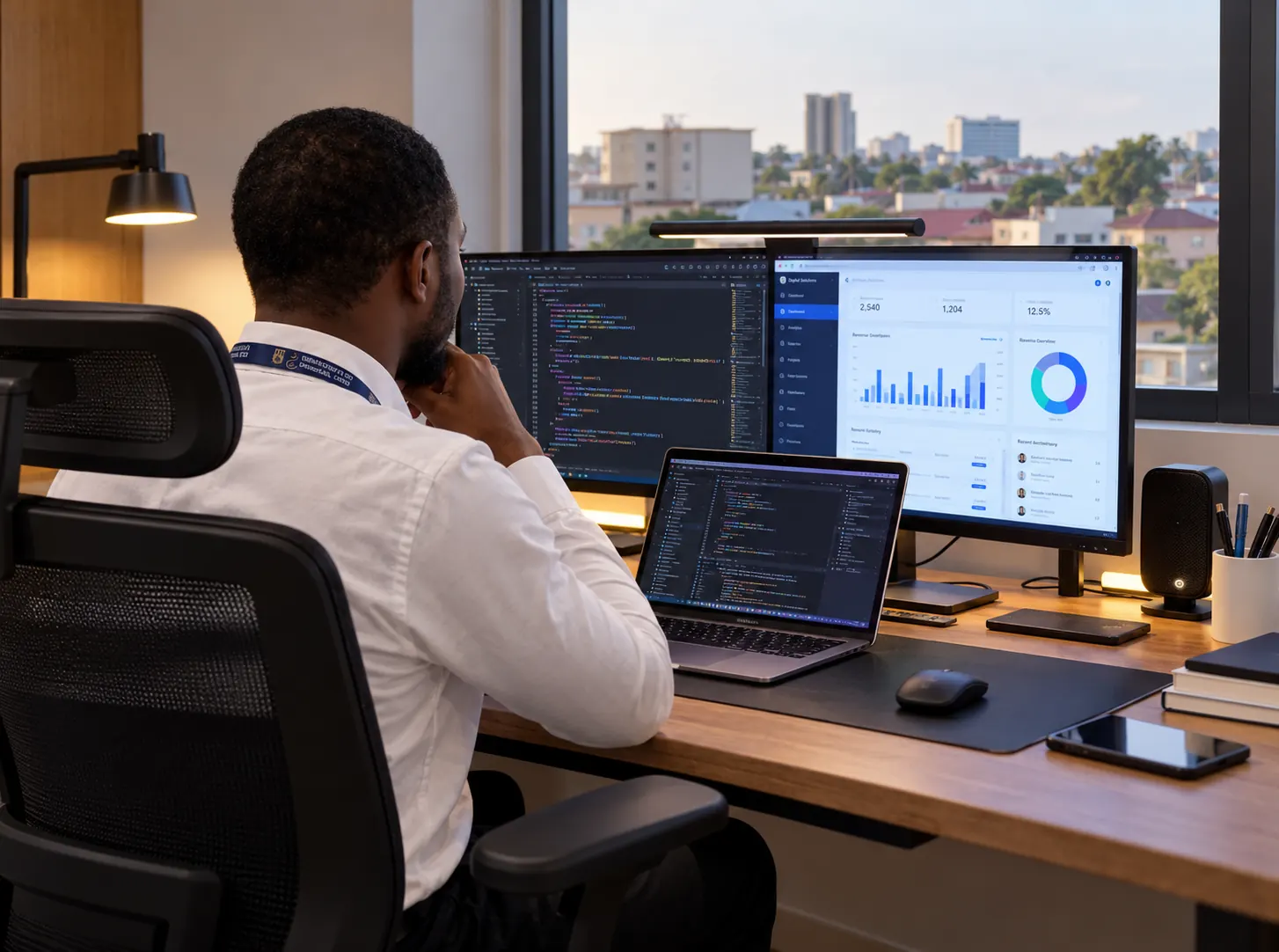 A developer wearing a white shirt and university lanyard working at an office desk in Ghana